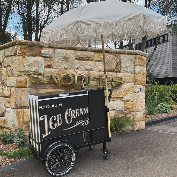Elegant black ice cream cart with fringe umbrella, supplied by PromoWheels, perfect for serving ice cream in style at any occasion or market.