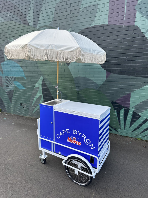 Colourful ice cream cart with a stylish umbrella, supplied by PromoWheels, designed for outdoor events and festivals. Ideal for showcasing ice cream and drinks at markets.