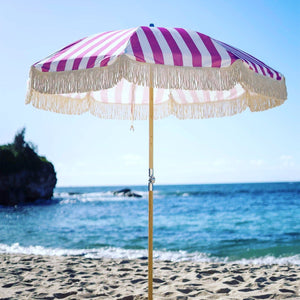 Pink striped beach umbrella with tassels, designed by PromoWheels, showcasing high quality and a vibrant design perfect for sunny days at the beach.