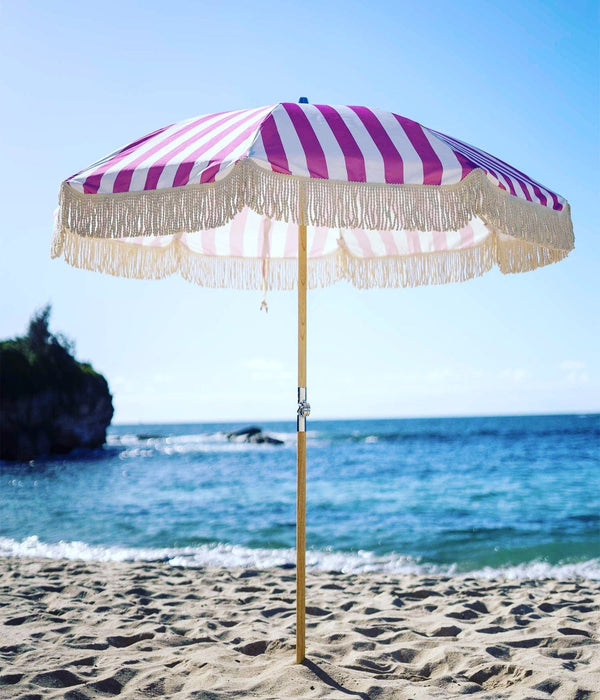 Pink striped beach umbrella with tassels, designed by PromoWheels, showcasing high quality and a vibrant design perfect for sunny days at the beach.