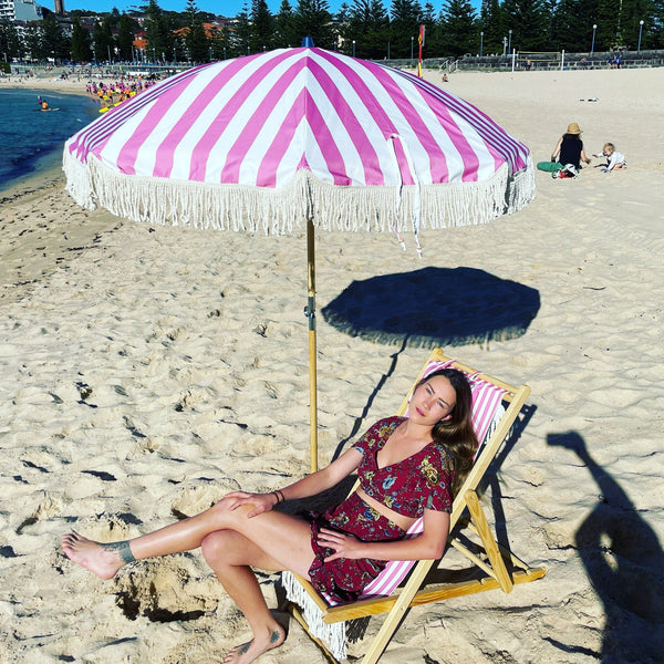 Beachgoer relaxing under a pink striped tasselled beach umbrella by PromoWheels, representing high-quality Australian design for sun protection.